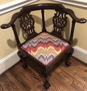 Corner chair with decorative back and ball-and-claw feet, featuring an upholstered seat with a colorful zigzag pattern.